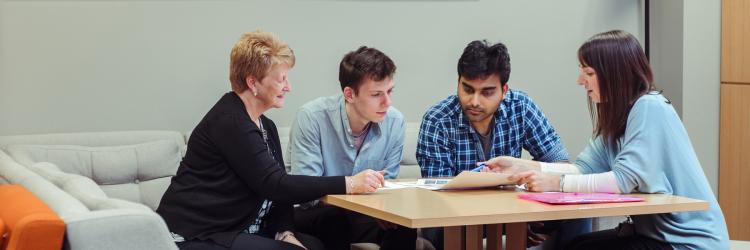 Four people sat round a table talking through news items paperwork