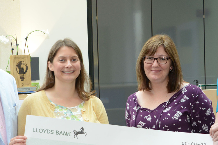 Four people holding a large check smiling at the camera in a reception area