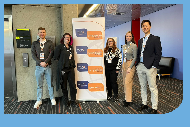 5 young Euan MacDonald Centre researchers standing alongside the MND Association Symposium banner