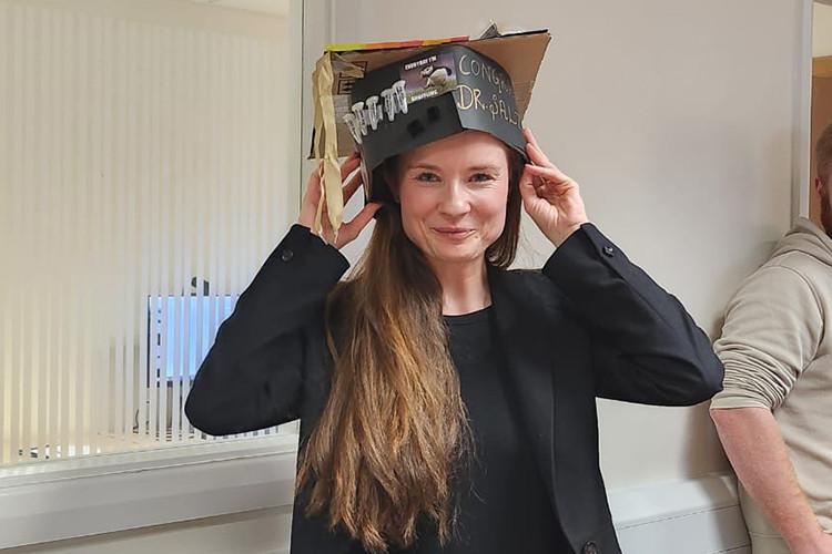Dr Andrea Salzinger smiling and wearing a home-made graduation hat