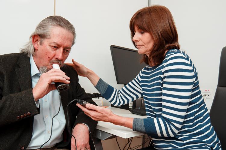 A patient does a spirometery test (appuratus for measuring lung capacity) carried out by a research nurse in a clinic room
