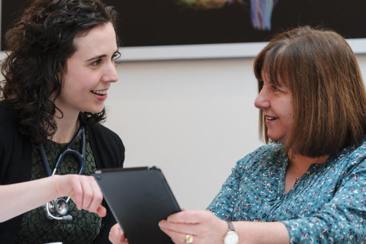 Doctor and patient picture happily talking while patient holds an iPad and Doctor is pointing at the screen
