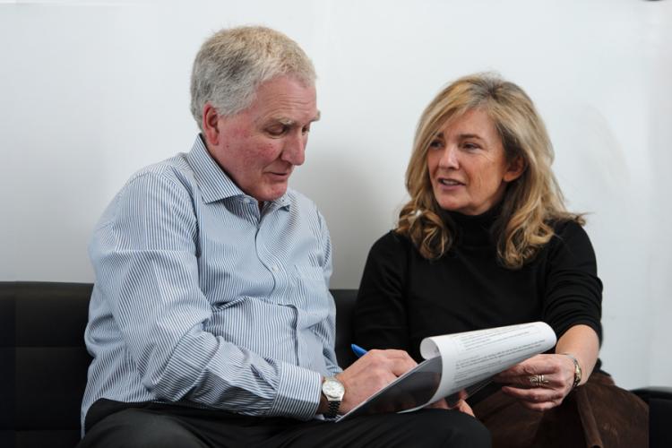 A couple are sat in a clinic waiting room, looking at medical documents