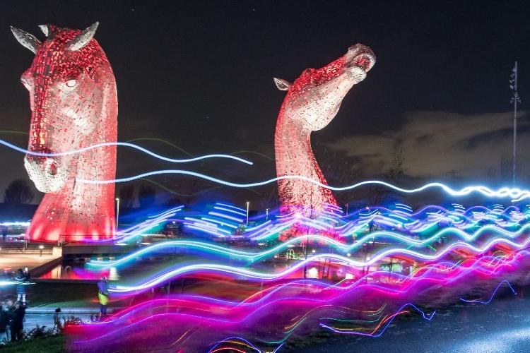 The Kelpies - statues at the Helix Park in Falkirk. The statues are illuminated red against the night sky.