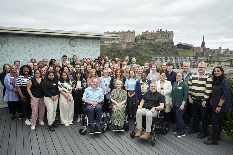 MND SMART trial team and associated researchers at the annual meeting 2024: a group of approximately 100 people outside, with Edinburgh Castle in the background