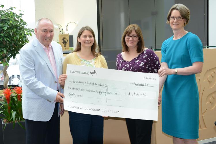 Four people holding a large check smiling at the camera in a reception area