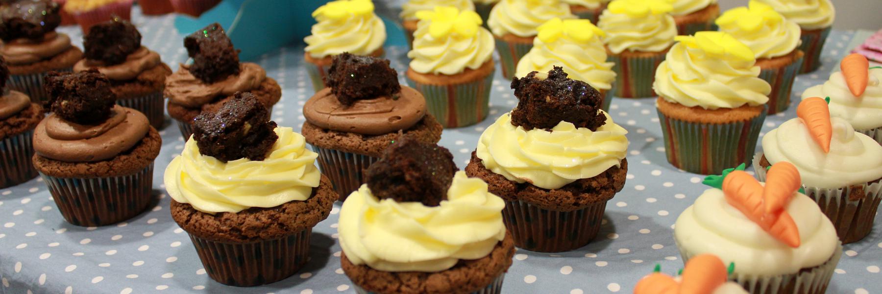 A close up of chocolate and carrot cake cupcakes on a blue polka dot table cloth at a bake sale raising funds for the Euan MacDonald Centre