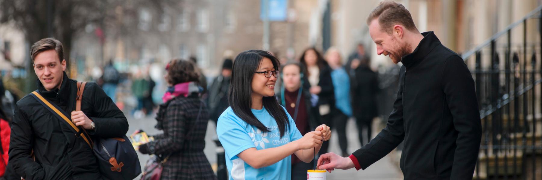 Man on a street putting money into a collecting can
