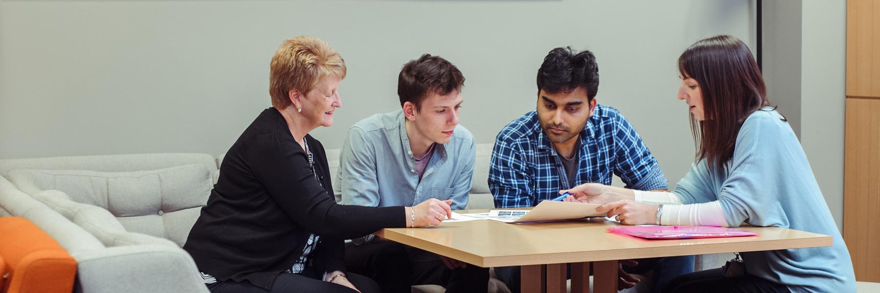 Four people sat round a table talking through news items paperwork