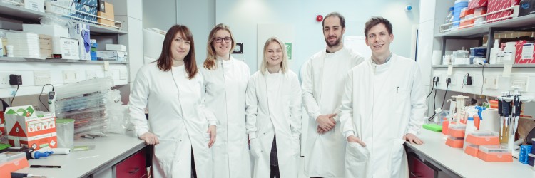 five researchers wearing lab coats standing in a laboratory