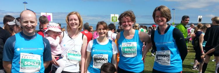 Five runners wearing Euan Macdonald t-shirts and running numbers, smiling at the camera