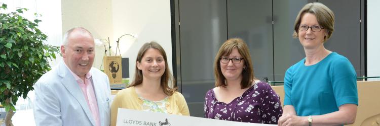Four people holding a large check smiling at the camera in a reception area