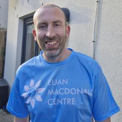 Graeme Barry standing smiling, wearing a Euan MacDonald Centre T-shirt