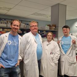 David Story (2nd from left) with team mates (L-R) Paul Baxter, Sophie Hawkins and James Cooper, wearing Euan MacDonald Centre T-shirts and lab-coats, and standing together in a lab.
