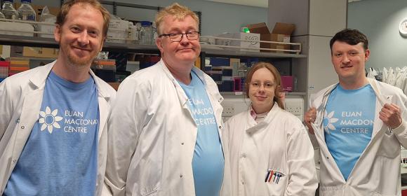 David Story (2nd from left) with team mates (L-R) Paul Baxter, Sophie Hawkins and James Cooper, wearing Euan MacDonald Centre T-shirts and lab-coats, and standing together in a lab.