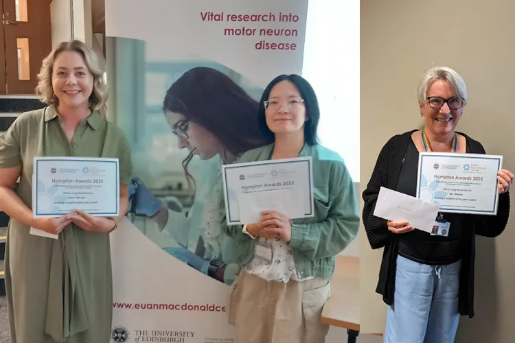 Three people standing indoors,smiling and holding a certificate, with a Euan MacDonald Centre banner in the background